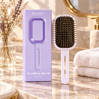 A 3D airbag hairbrush shown next to its lavender packaging box on a marble bathroom counter, with a folded white towel and dried flowers in the background.