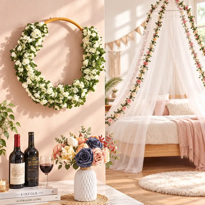 A floral wreath made of white roses and green leaves hangs on a beige wall in a styled bedroom scene. The room includes a bed with a sheer canopy decorated with pink flowers, books, wine bottles, and a vase of mixed flowers on a table.
