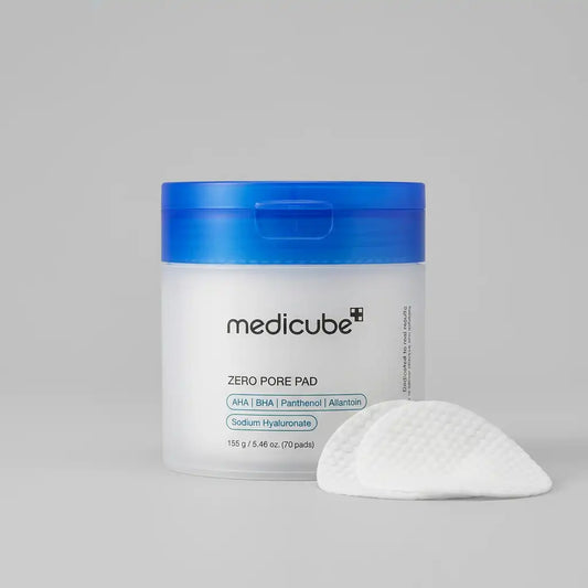 A jar of medicube Zero Pore Pad with a translucent white body and a bright blue lid, shown next to a single white textured pad on a neutral gray background.