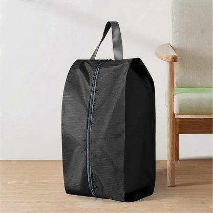 A black zippered storage bag with a top handle, standing on a light wood floor next to a wooden chair with a light green cushion.