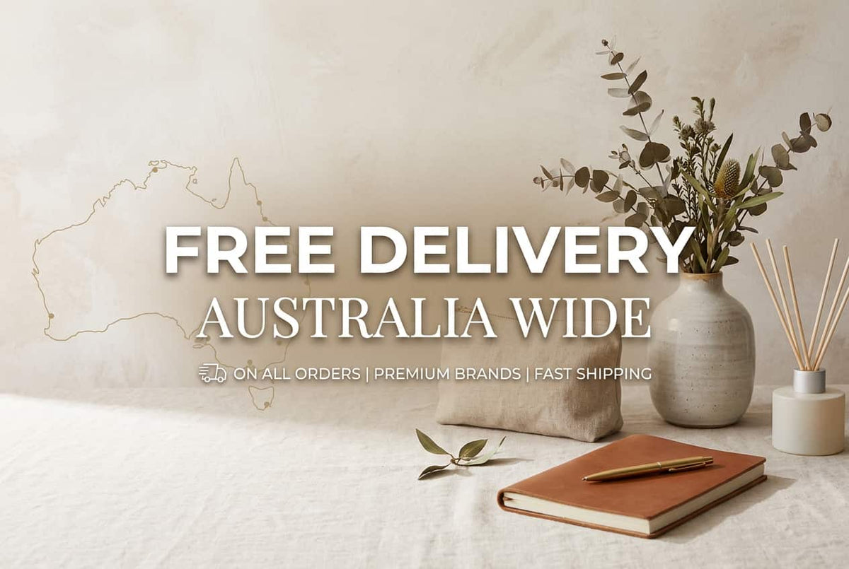 Promotional banner with the text 'FREE DELIVERY AUSTRALIA WIDE' over a styled tabletop scene. The scene includes a beige textured vase with dried eucalyptus stems, a small reed diffuser, a brown notebook with a gold pen, and a small fabric pouch on a light surface.