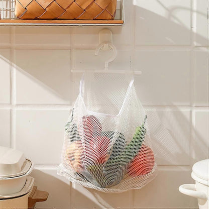 A white mesh hanging grocery bag suspended from a hook on a tiled kitchen wall, filled with colorful produce.